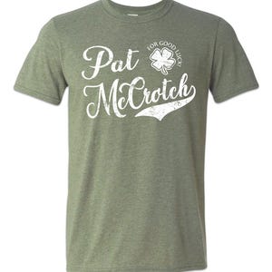 May include: A green t-shirt with a white distressed graphic that says "Pat McCroch" with a shamrock and the text "For Good Luck!" above the name.