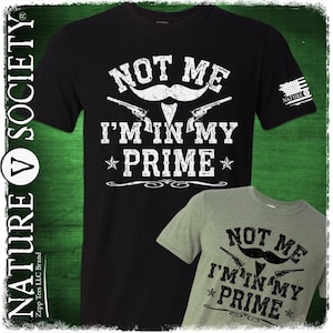 May include: Black and green t-shirt with a white graphic that says "Not Me I'm In My Prime" with a mustache and two pistols. The graphic is surrounded by a decorative border.