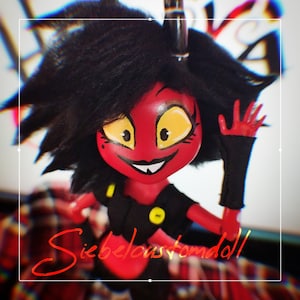 Op de afbeelding: Een aangepaste pop met een rood gezicht, gele ogen en zwart haar. De pop draagt een zwarte outfit met gele accenten. De pop zwaait met een rode hand. De tekst "Siebelouscustomdoll" is in rode cursieve letters geschreven.
