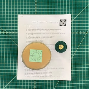 May include: A craft setup for Tenerife lace making. It includes a round wooden pillow with a pattern, a spool of green thread, and instructions. The instructions detail how to create the lace motif with 16 pins.