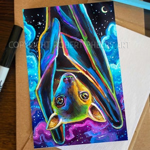 May include: A colorful painting of a bat hanging upside down against a dark blue and purple starry night sky. The bat is painted in shades of blue, green, yellow, and orange. The painting is framed in a white border.