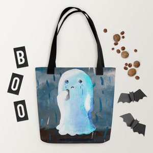 May include: A blue tote bag featuring a sad ghost illustration with tears, set against a rainy background. The bag has black handles and the word "BOO" in black letters. Decorative elements include paper bats and nuts.