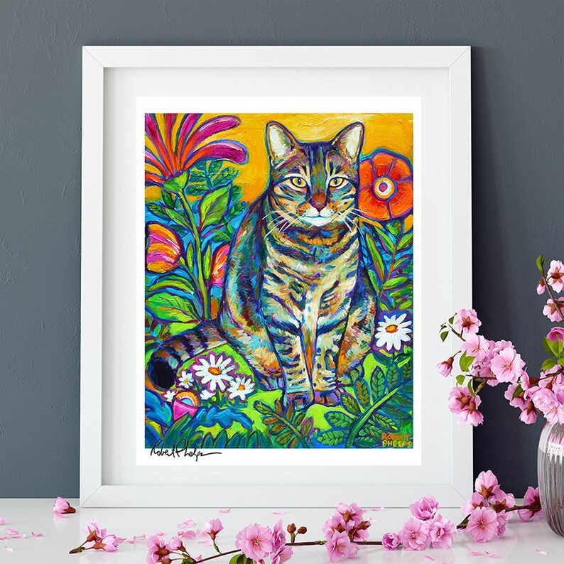 May include: A colorful painting of a tabby cat sitting in a garden with flowers. The cat is surrounded by bright green leaves and flowers in shades of pink, red, orange, and yellow. The artist's signature, "Robert Phelps", is visible in the bottom left corner.