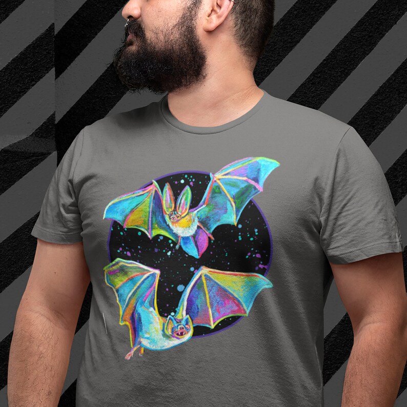 May include: A gray t-shirt with a colorful illustration of two bats flying in a circle against a black background with white stars. The bats are iridescent with blue, green, purple, and pink colors.