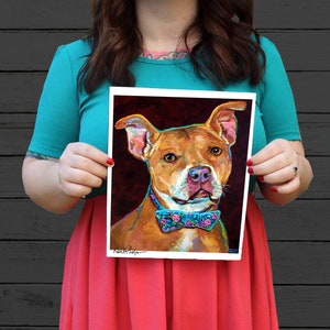 Puede incluir: Una pintura colorida de un pitbull marr&oacute;n y blanco con una pajarita floral azul y rosa. El perro mira directamente al espectador con una expresi&oacute;n seria. El fondo es de color rojo oscuro.