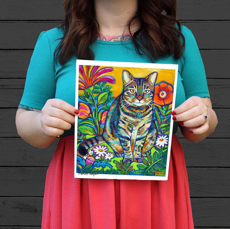 May include: A colorful painting of a tabby cat sitting in a garden with bright flowers and green foliage. The cat has green eyes and a white patch on its chest. The background is a bright yellow.