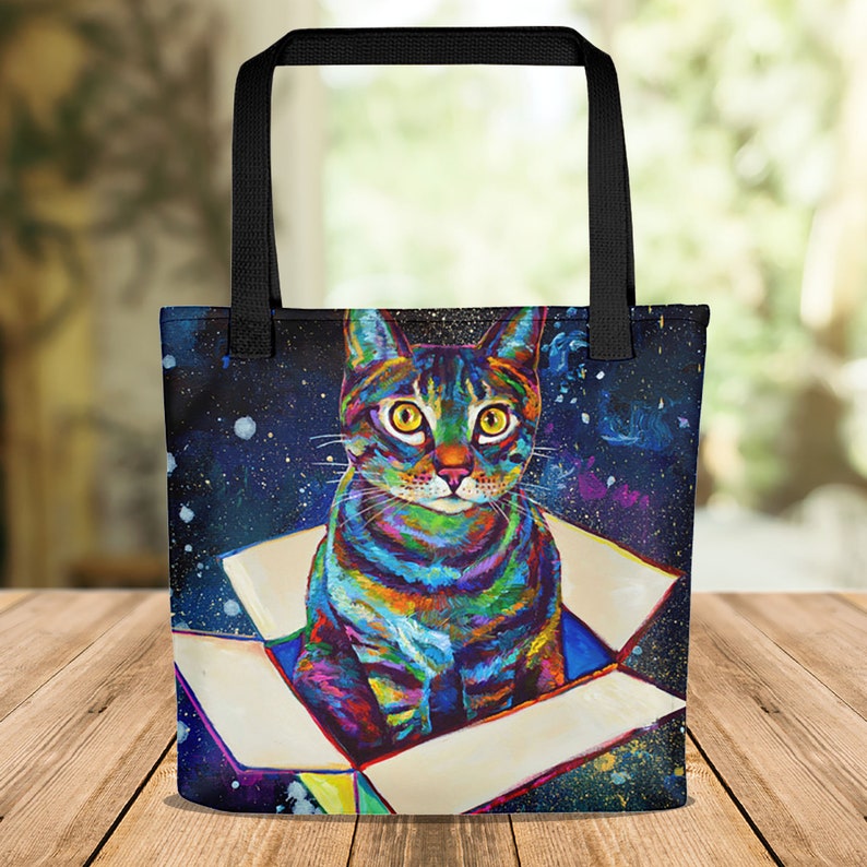 May include: A colorful tote bag with a psychedelic cat sitting in a box against a starry night background.