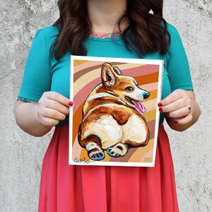 May include: A colourful painting of a corgi dog with a brown and white coat, sitting with its back to the viewer. The dog is on a background of brown and orange stripes. The painting is signed "Robert Phelps".