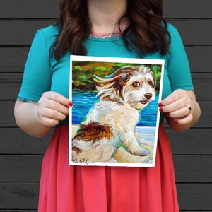 May include: A painting of a white and brown dog with its tongue sticking out. The dog is in a boat and the water is blue. The painting is signed "Robert Phelps" in the bottom left corner and "Phillip" in the bottom right corner.