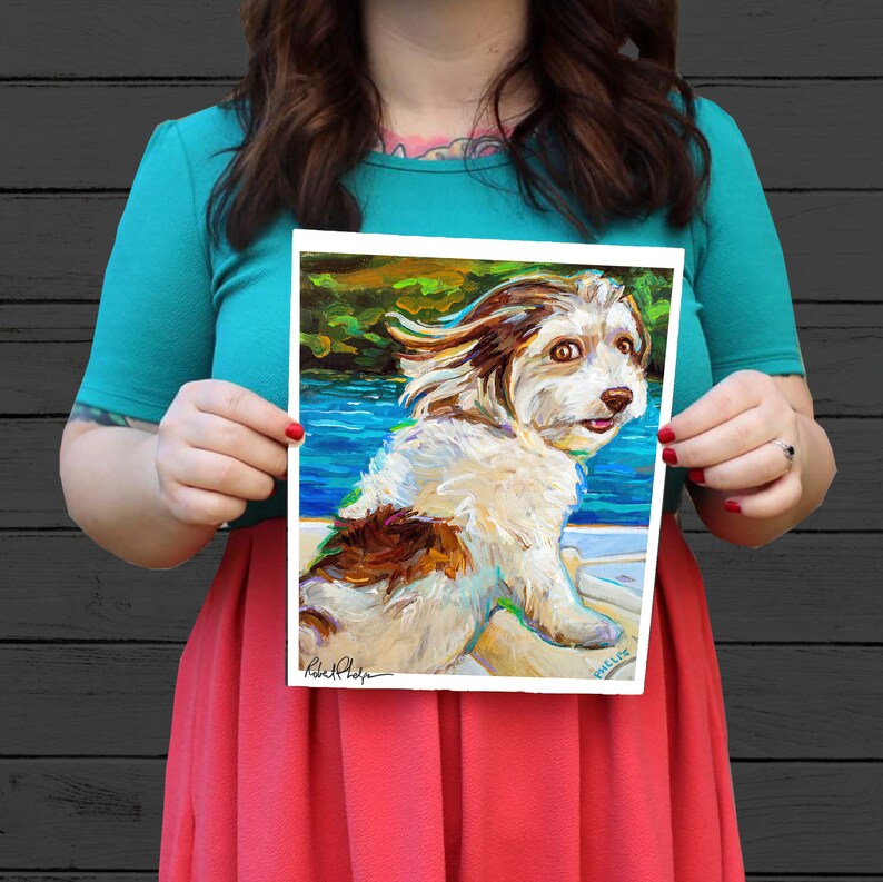 May include: A painting of a white and brown dog with its tongue sticking out. The dog is in a boat and the water is blue. The painting is signed "Robert Phelps" in the bottom left corner and "Phillip" in the bottom right corner.