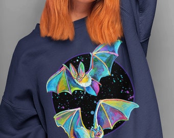 May include: A navy blue sweatshirt with a circular design featuring two iridescent bats flying against a black background with white stars. The bats have a rainbow-like colour scheme.