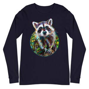 May include: Navy blue long-sleeve shirt featuring a colorful raccoon illustration within a green and blue circular frame. The raccoon is depicted with detailed fur and expressive eyes, set against a backdrop of foliage.
