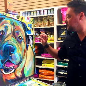 May include: A colorful painting of a dog's face, with bright blue, green, yellow, and pink colors. The artist is painting the dog's face in a pet store.