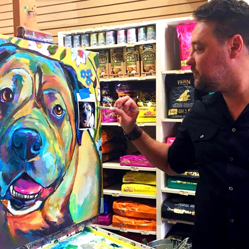 May include: A colorful painting of a dog's face, with bright blue, green, yellow, and pink colors. The artist is painting the dog's face in a pet store.