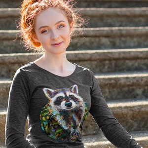 May include: Dark gray long-sleeve shirt featuring a colorful raccoon graphic. The raccoon has a detailed, artistic design with a variety of colors. The shirt has a scoop neck and long sleeves. The background is a set of concrete steps.