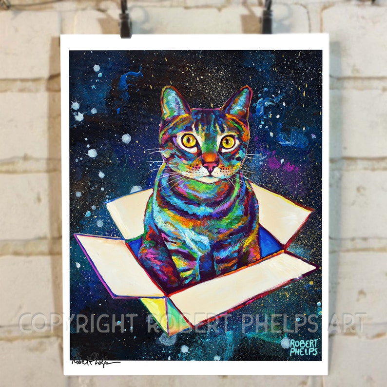 May include: A colorful, abstract painting of a cat sitting in a box against a dark blue, starry background. The cat's fur is painted in shades of blue, green, yellow, and orange. The box is white with a yellow interior. The painting is signed "Robert Phelps" in the bottom right corner.