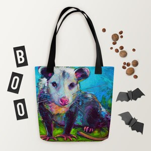 May include: A tote bag featuring a colorful painting of a possum with a blue, green, and purple background. The possum is looking directly at the viewer with a curious expression.