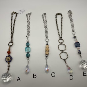 May include: Five decorative cat charms with various designs. Charms include a floral design, blue and green beads, wooden beads, geometric shapes, and a crystal ball. Each charm has a chain and a crystal pendant.