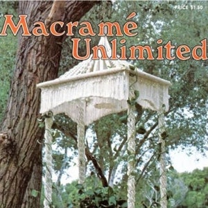 May include: A white macrame plant hanger with a square top and fringe. The hanger is suspended from a tree branch and holds a potted plant. The image is from a book titled "Macrame Unlimited" and features the project "The Plant Cradle".