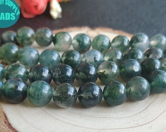 May include: A strand of green moss agate beads, each bead is round and has a mottled green and white pattern. The beads are arranged in a circle on a wooden surface.