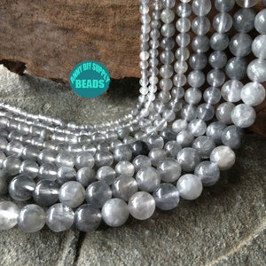 Könnte beinhalten: Eine Strähne durchscheinender grauer Edelsteinperlen mit einem leichten Schimmer. Die Perlen sind rund und glatt und liegen in einem lockeren Haufen. Die Perlen haben einen Durchmesser von etwa 10 mm.