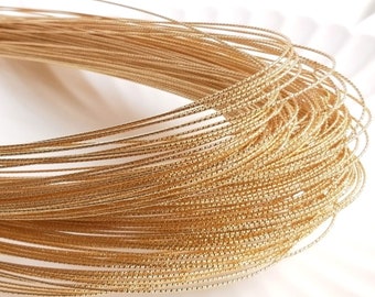 May include: A close-up of a spool of gold-colored wire with a textured surface. The wire is tightly wound and appears to be very fine.