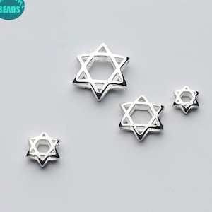 Peut inclure: Quatre breloques en forme d'étoile de David argentées de différentes tailles. Les breloques sont creuses et présentent un design délicat.