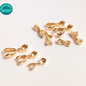 May include: A group of 10 gold-toned metal pendant clasps, also known as bail clasps, for jewellery making. The clasps are in various sizes and are scattered on a white surface.