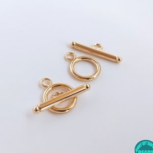 Può includere: Due chiusure a scorrimento in metallo dorato per la creazione di gioielli. Una chiusura ha un anello rotondo e una barra dritta, mentre l'altra ha un anello rotondo e una barra curva.