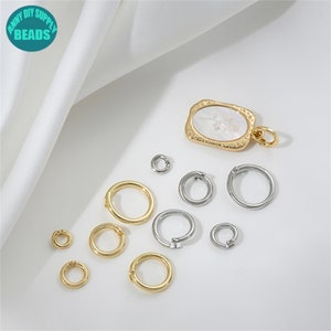 May include: Assortment of gold and silver jump rings, perfect for jewelry making. The rings are of various sizes and are displayed on a white surface.  A gold pendant with a white shell inlay is also included.