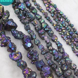 May include: A close-up of several strands of iridescent black gemstone beads. The beads are faceted and have a rough, natural texture. The beads are strung on a clear thread and are arranged in a row.