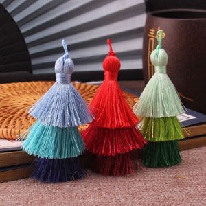 May include: Three layered tassels in blue, red, and green. Each tassel has three layers of colour, with the top layer being the lightest and the bottom layer being the darkest. The tassels are made of soft, silky yarn and are perfect for adding a touch of colour and texture to your crafts.