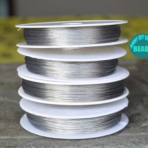 May include: Four spools of silver-colored jewelry wire, wound around white spools. The spools are stacked on top of each other. The label on the top spool reads "Anny DIY Supply Beads".