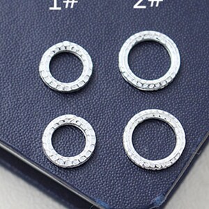 May include: Four silver jump rings, two larger and two smaller, on a blue surface. The rings are labelled "1#" and "2#" in white text.