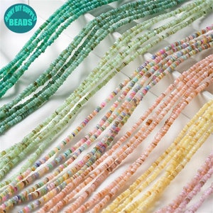 Op de afbeelding: Assortiment van kleurrijke zaadkraaltjes in verschillende tinten groen, roze en geel. De kralen zijn in rijen op een wit oppervlak gerangschikt.