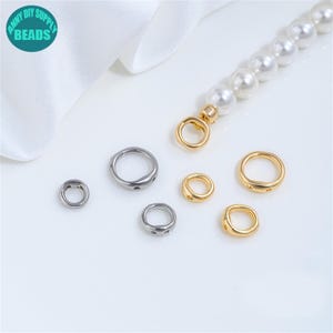 Puede incluir: Un surtido de suministros para la fabricación de joyas, que incluye anillos de metal plateado y dorado, y un collar de perlas con un cierre dorado. Los anillos varían en tamaño y diseño, perfectos para crear collares y pulseras. La imagen incluye un logotipo turquesa y blanco.