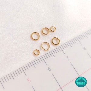 May include: A set of six gold jump rings of varying sizes, measured against a ruler with markings in centimeters. The jump rings are used for jewelry making and crafting.
