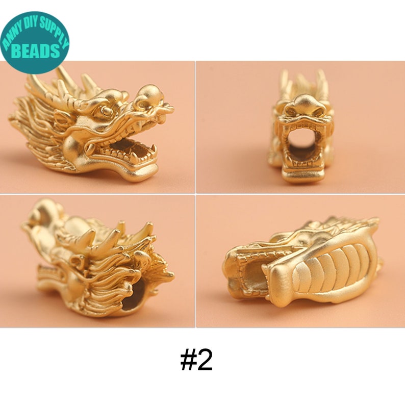 May include: Gold-colored dragon head charm with intricate details. The charm has a hollow center and is designed to be used as a bead or pendant.