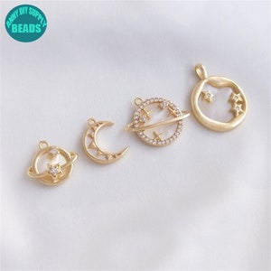 May include: Four gold-tone metal charms with a celestial theme. The charms feature a crescent moon, a planet with a ring, and two different versions of a planet with stars.