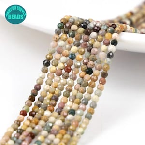 May include: A strand of multi-colored gemstone beads. The beads are faceted and have a variety of brown, green, and pink tones. The beads are strung on a clear thread.
