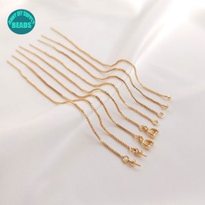 Puede incluir: Un conjunto de diez extensores de cadena dorados, cada uno con un estilo de cierre diferente. Los extensores están dispuestos en una fila sobre una superficie blanca.