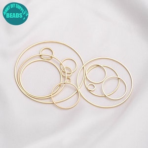 Pode incluir: Um conjunto de 10 argolas de metal douradas de tamanhos diferentes. As argolas estão dispostas em um padrão aleatório sobre uma superfície branca.