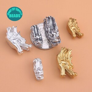 May include: Five dragon head charms, two silver and three gold, for jewelry making. The charms are detailed and have a textured finish.