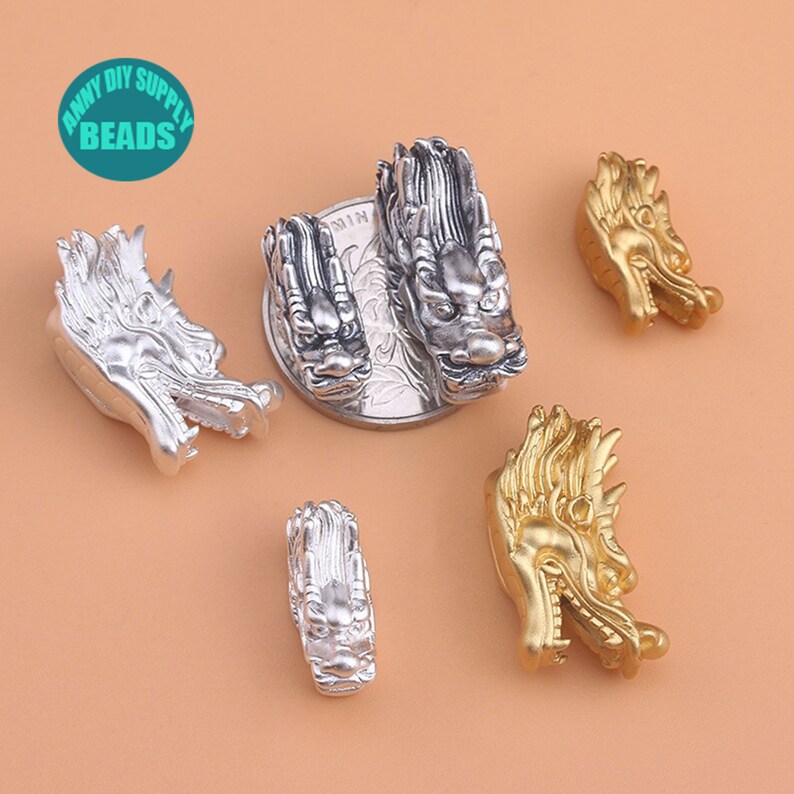 May include: Five dragon head charms, two silver and three gold, for jewelry making. The charms are detailed and have a textured finish.