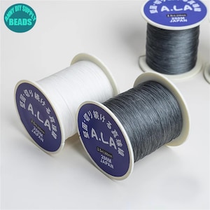 Puede incluir: Dos carretes de hilo blanco y gris etiquetados "A.L.A. 200M JAP&Oacute;N".