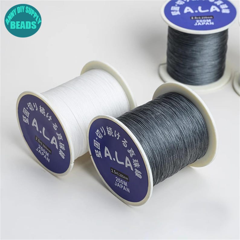 Puede incluir: Dos carretes de hilo blanco y gris etiquetados "A.L.A. 200M JAP&Oacute;N".