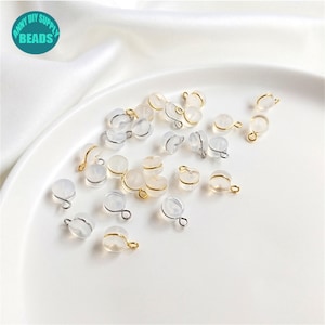 May include: A collection of clear plastic beads with gold-coloured metal loops. The beads are scattered on a white surface.