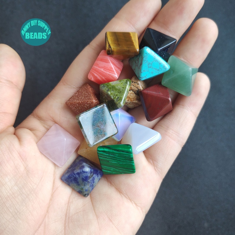 May include: A collection of 15 small, pyramid-shaped crystals in various colours, including pink, green, blue, red, brown, and white. The crystals are arranged in a hand, with the tips of the pyramids facing up.
