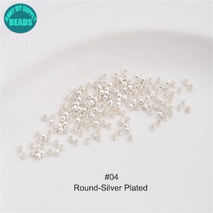 May include: A close-up of a pile of small, round, silver-plated beads. The beads are scattered on a white surface. The text "#04 Round-Silver Plated" is printed below the beads.