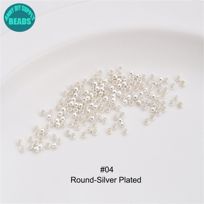 May include: A close-up of a pile of small, round, silver-plated beads. The beads are scattered on a white surface. The text "#04 Round-Silver Plated" is printed below the beads.